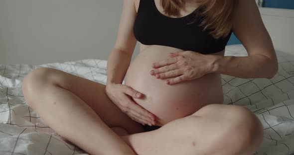 A Young Pregnant Woman Strokes Her Belly with Her Hands