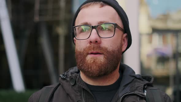 Close Up View of Thoughtful Guy in Glasses Walking at City Street. Portrait of Serious Bearded Man