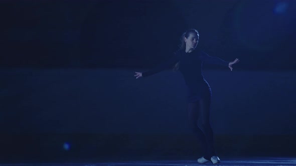 Professional Figure Skating Artist Slides and Spins on Ice Arena in Rays of Blue Light