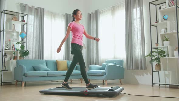 Side View Of Asian Woman Training On Walking Treadmill And Looking Smart Watch At Home