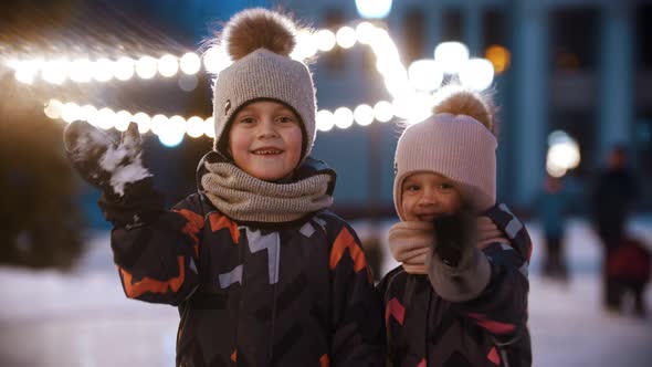 Two Little Kids Standing on Public Ice Rink and Waving with Their Hands - Looking in the Camera