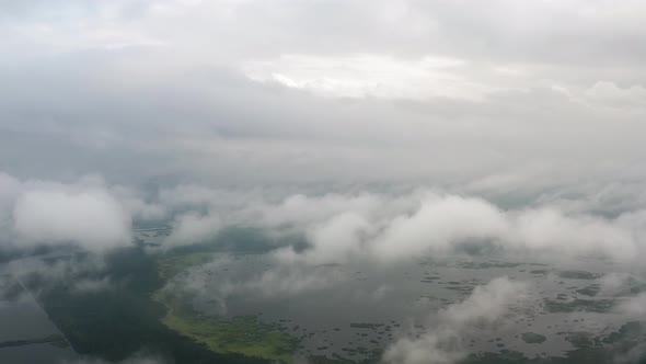 Aerial Top View Drone Flies Through Fluffy Rain Clouds Rolling Over Green Forest By Beautiful Lake