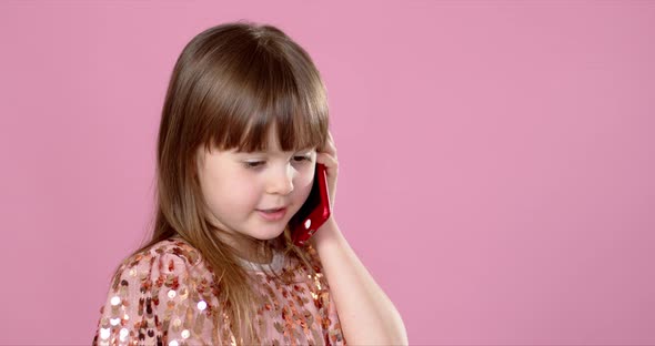 Cheerful Little Blonde Kid Girl 6-7 Years Old in Sequin Dress Talking on Mobile Phone