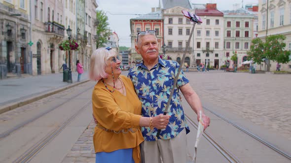 Senior Old Tourists Man with Woman Walking in City with Smartphone on Selfie Stick and Taking Photos