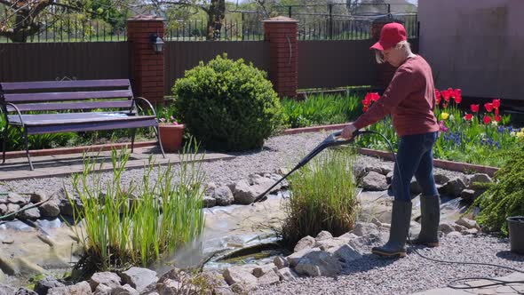 Woman Cleans Garden Pond Bottom From Dirt and Silt with Highpressure Washer