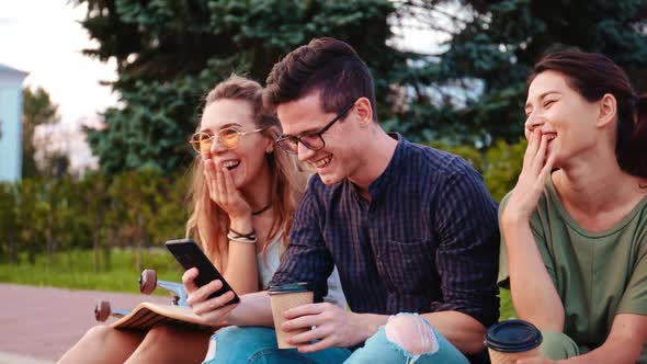 Happy Smiling Teenage Friends Laughing Outside at Something in Smartphone or Mobile Phone