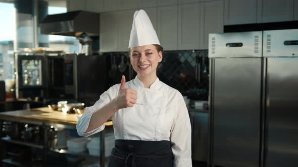 Professional kitchen portrait: Female Chef showing thumbs up and smiling