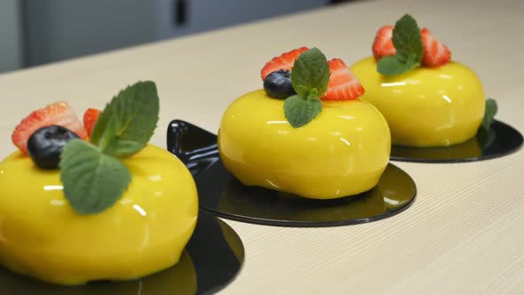 Dolly Shooting a Row of Yellow Mousse Cakes with Strawberries and Blueberries