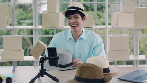 Smiling Asian man influencer reviewing fedora hat and selling a product online.