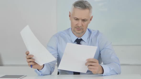 Senior Businessman Reading Documents in Office Contract