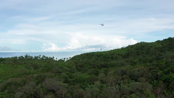 Helicopter with cargo hanging from cable flying towards helipad on remote island