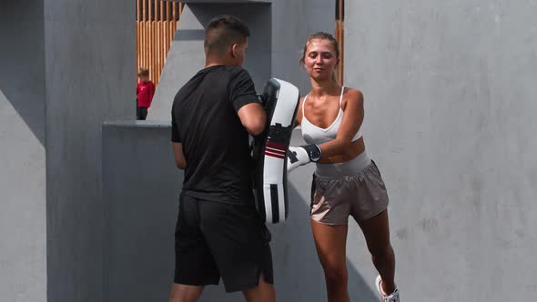 Young Woman in White Top Having a Boxing Training with Her Coach Outside Kicking the Portative