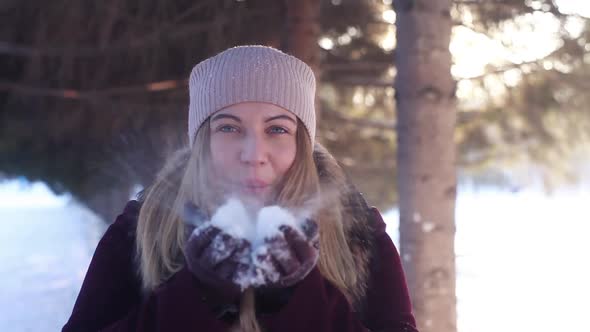 Young Happy Girl Blowing Snow From the Varek in the Open Air in Sunny Winter Weather