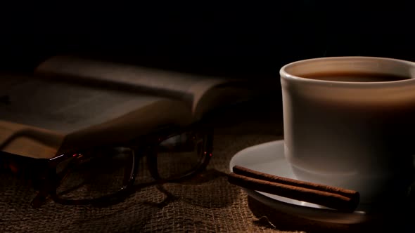 Hot Coffee and Book with Glasses, Cinnamon on Sacking, Black Background