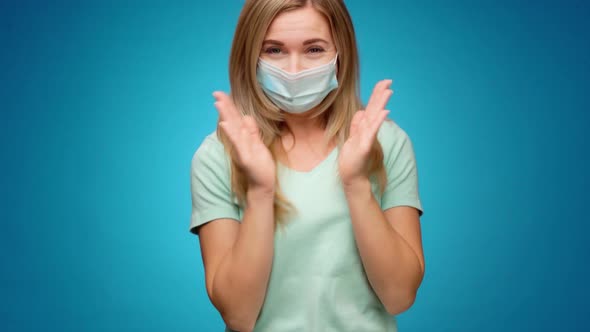 Woman in Medical Mask on Face is Very Happy and Claps Her Hands Against Blue Background