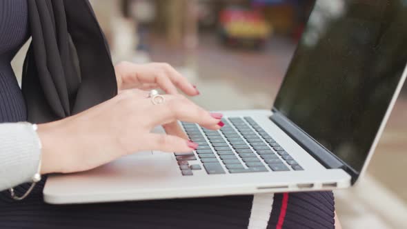 Close Up Shot Of Woman Sat Outside Typing/Working On Her Laptop As People Walk Past