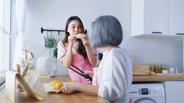 Asian lovely family, young daughter look to old mother cook food, bake croissant on table in kitchen