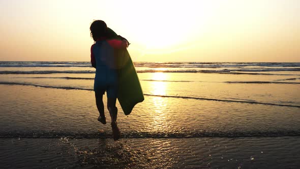 Little Girl is Running on the Sea to Waves Holding Surfboard in Her Hands