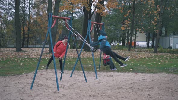 Happy Boy and Girl is Swaying on Swing in Park at Autumn Day and Jumping Out in Slow Motion. 