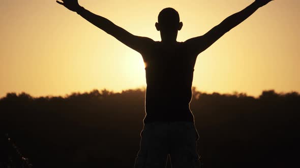 Silhouette of Young Man Against Sunset Raising Hands Sides and Up. Slow Motion