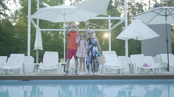 Portrait Happy Mature Couple with Little Granddaughter Standing at the Swimming Pool and Wave