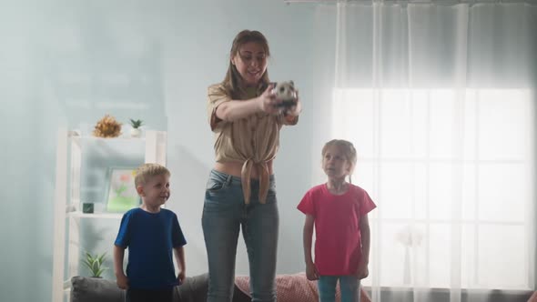 Woman Lifts Piggy Bank Over Head with Kids in Living Room