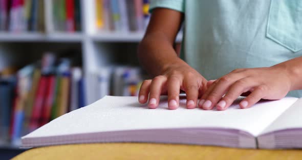 Mid-section of school kid reading a braille book in classroom at school