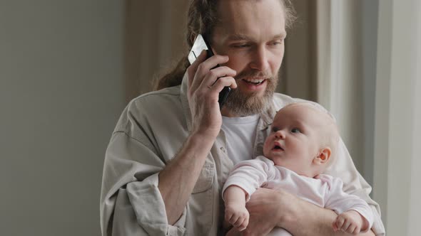Bearded Caucasian Man Father Adult Multitasking Dad Holding Baby at Home Talking on Phone with