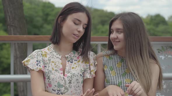 Two Attractive Girls Sitting Outdoors Together Chatting About New Manicure