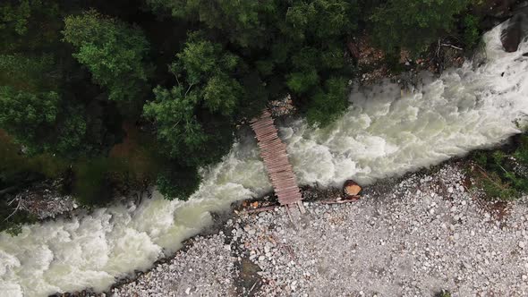 Wooden Bridge Over River Running Between Forest and Rocks