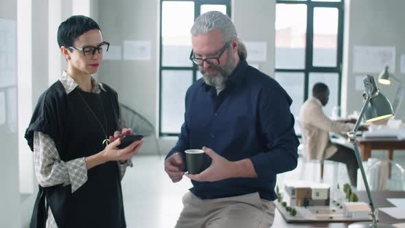 Two Middle Age Colleagues Chatting over Coffee in Office