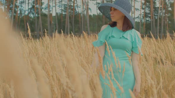 Young Woman in Dress and Hat Standing in Wheat Field