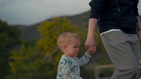 Blond Toddler Holds Mother Hand Walking on Beach at Twilight