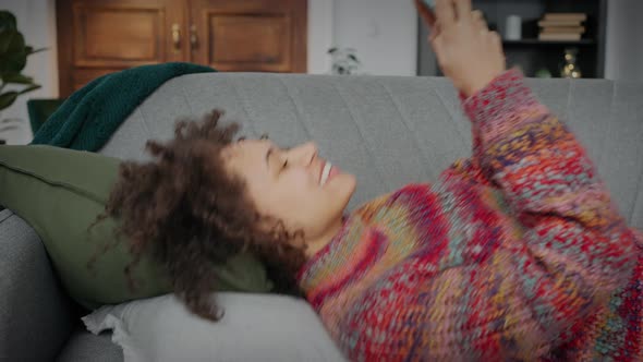 Young Carefree Curly African American Woman Falling on Bed and Web Browsing on Social Media on