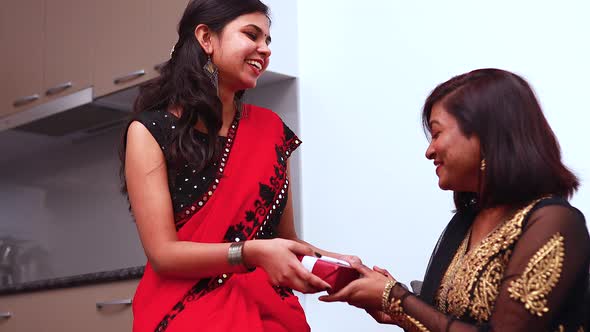 Cute Young Indian Woman Wearing Traditional Ethnic Clothes Giving Gift to a Sister in Living Room