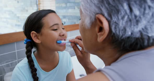 Grandmother helping granddaughter to brush her teeth in the bathroom 4k