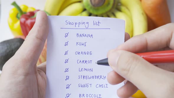 Hands hold shopping list checking with variety of colorful fresh fruits