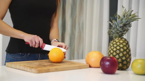 Female hands cutting orange on a wooden board. Woman in the kitchen. Healthy eating. Raw food.