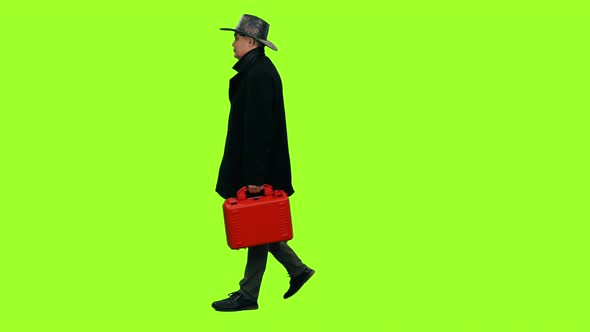 A Man in Cowboy Hat Walks with Red Case on Green Background