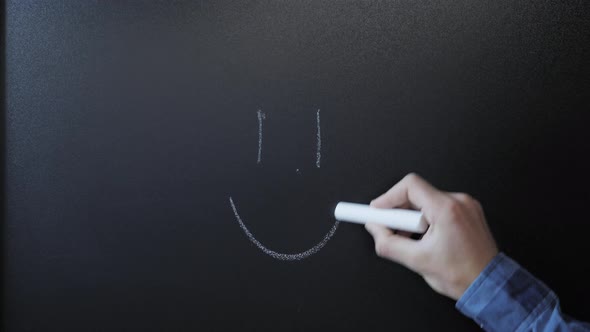 Hand drawing smile mark with white chalk on blackboard