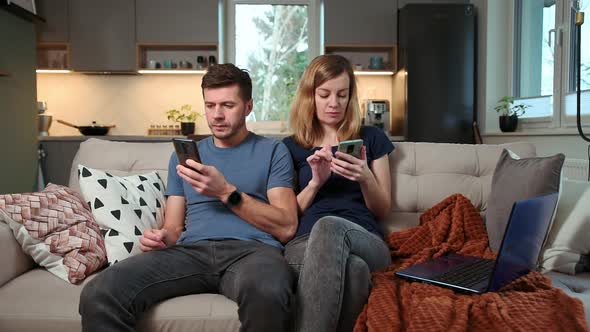 Family Couple Sitting on Sofa in Living Room and Using Smartphones