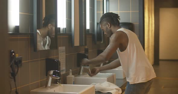 Side View of Young African American Man Approaching To Sink and Washing Face. Portrait of Relaxed