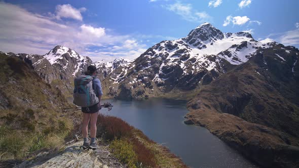 Pan, hiker overlooks alpine lake in snow capped mountain landscape, Routeburn Track New Zealand