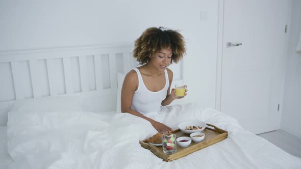 Woman with Smartphone in Bed Having Meal