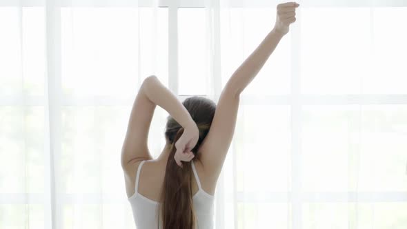 Beautiful young asian woman wake up and walking to window with open curtains and stretch.