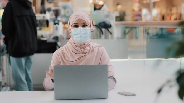 Young Muslim Businesswoman in Hijab in Medical Mask Sits in Public Place Working on Laptop Arab Girl