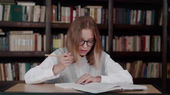 Schoolgirl Taking Notes From a Book at Library