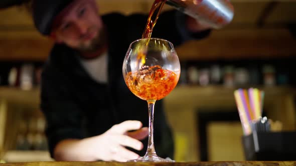 A Professional Bartender is Preparing an Alcoholic Cocktail with Ice Cubes to Customers at the Bar