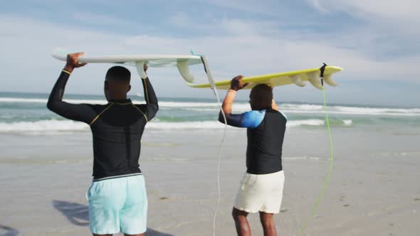 African american father and teenage son standing on beach holding surfboards on heads and talking