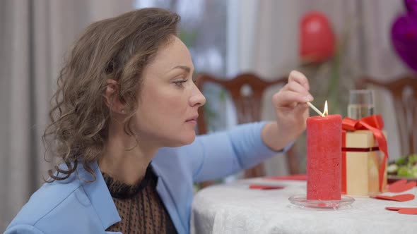 Side View of Beautiful Concentrated Woman Lighting Red Candle with Match